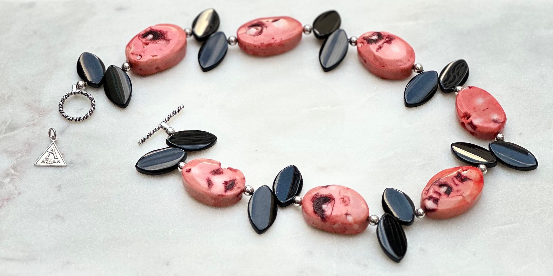 Necklace with pink and black stones on a white surface. Toggle clasp and pendant detail visible.
