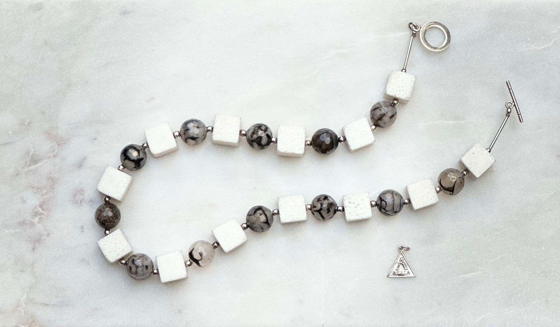 Necklace of white square and grey patterned beads with a triangle pendant on a marbled surface.
