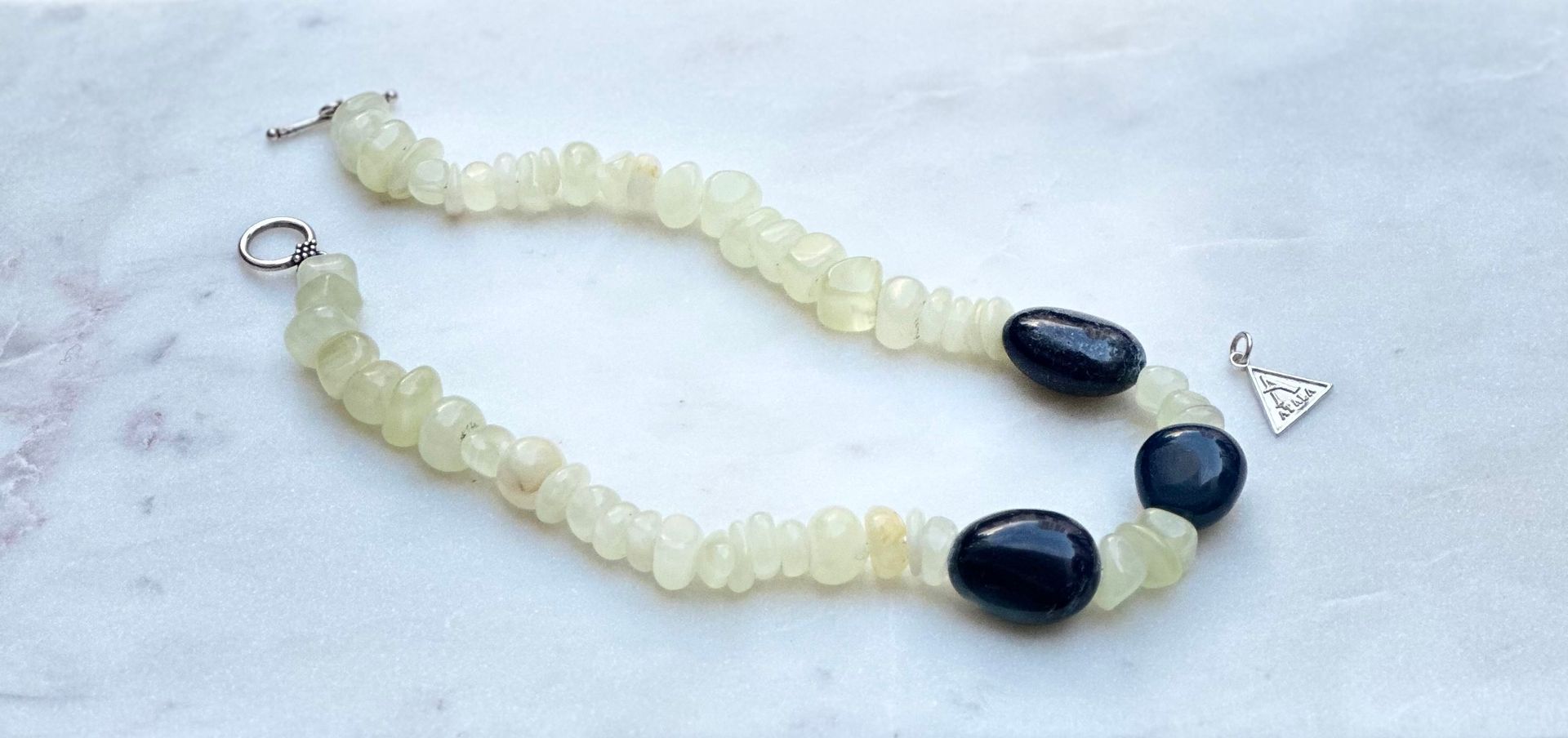 Bracelet with blue and yellow beads, with a silver clasp and a small triangle charm.