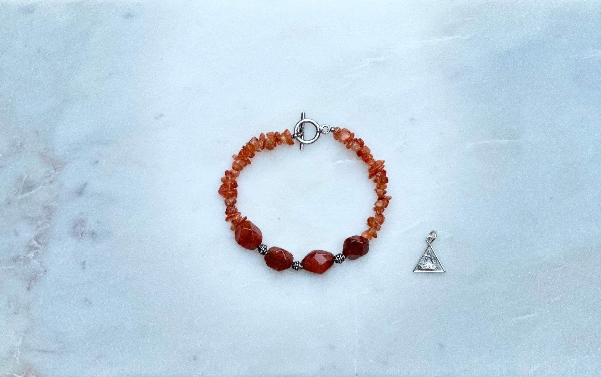 Orange beaded bracelet with silver clasp and small silver triangle charm on a white surface.