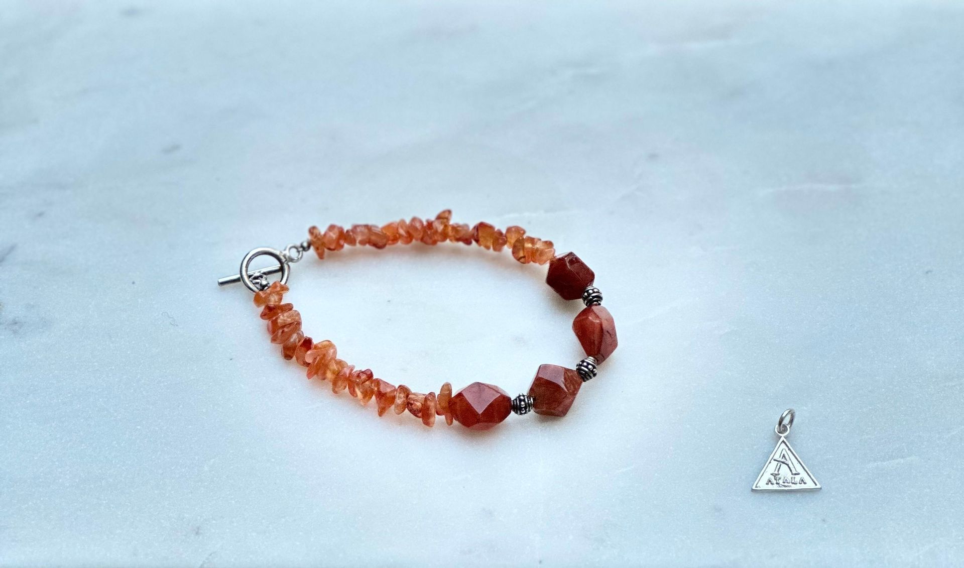 Orange beaded bracelet with silver clasp and small silver triangle charm on a white surface.