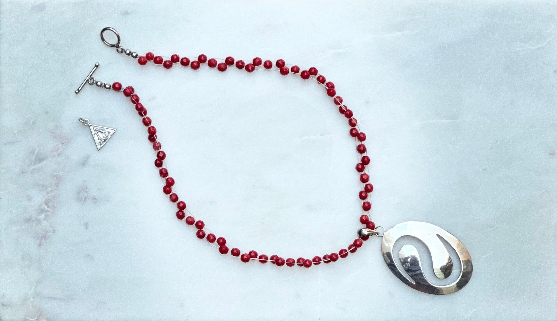 Red beaded necklace with a silver pendant on a light blue-white background.