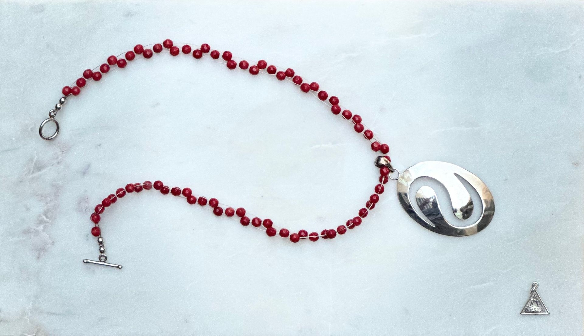 Red beaded necklace with a silver pendant on a light blue-white background.