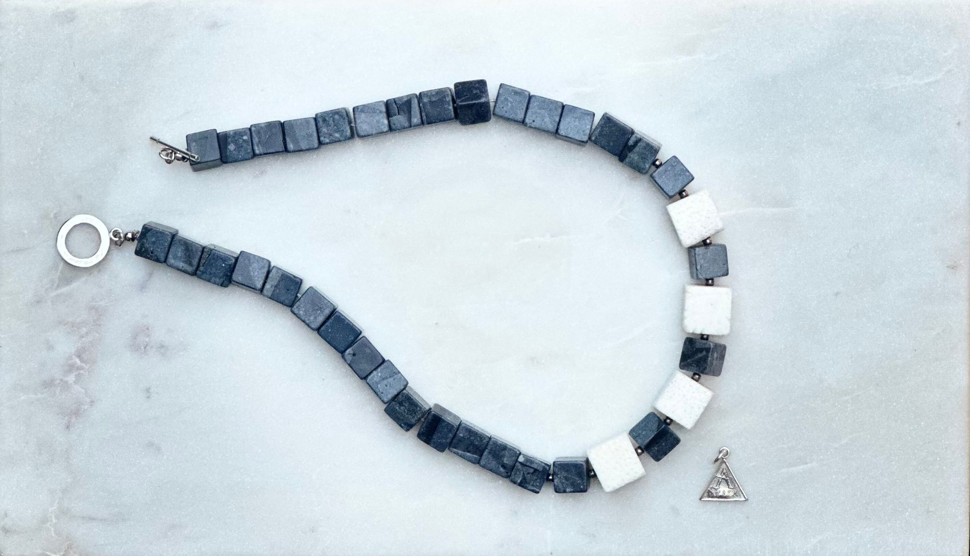 Bracelet made of square dark gray and white beads, with a clasp and small pendant.