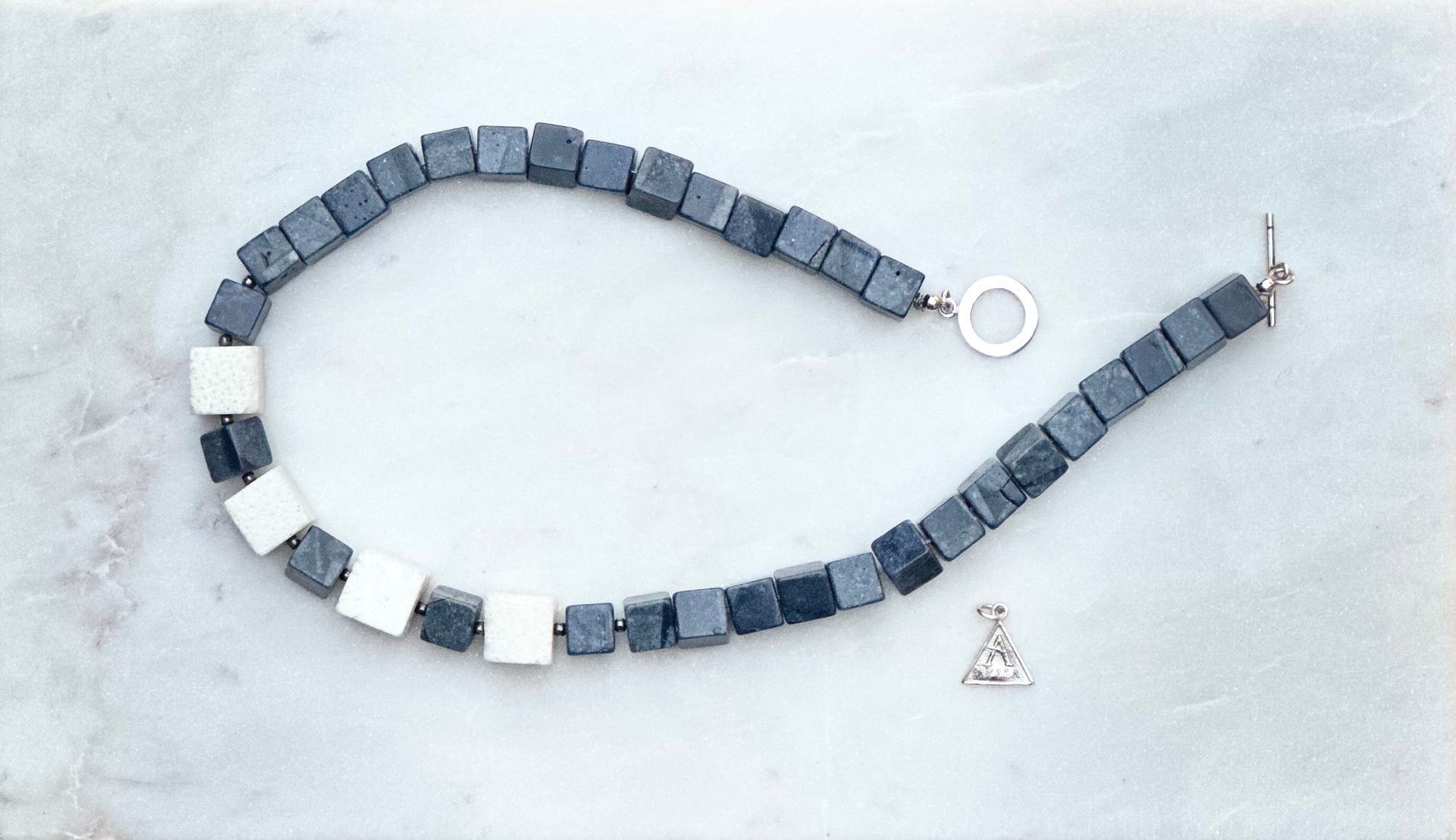Bracelet made of square dark gray and white beads, with a clasp and small pendant.