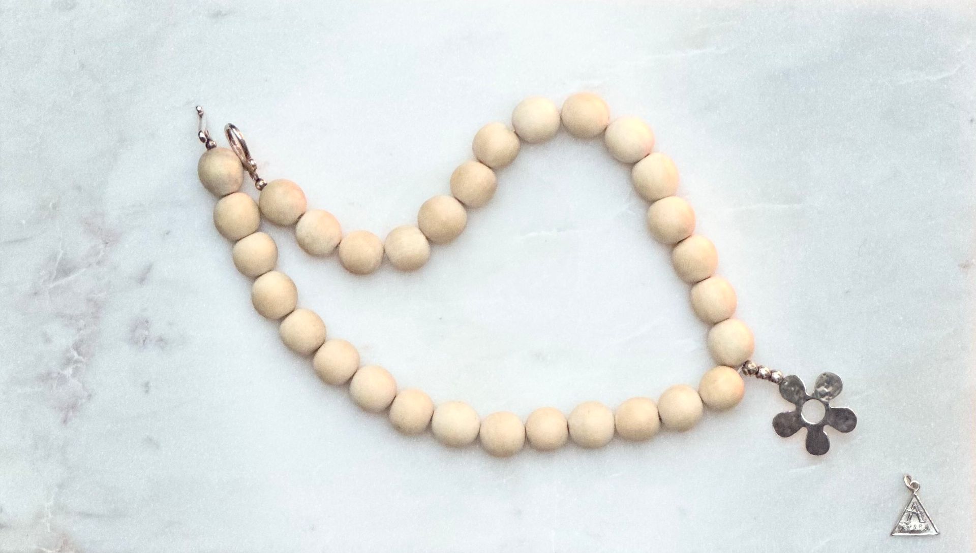 Beaded necklace with light wood beads and silver flower pendant. Small triangle charm to the side.