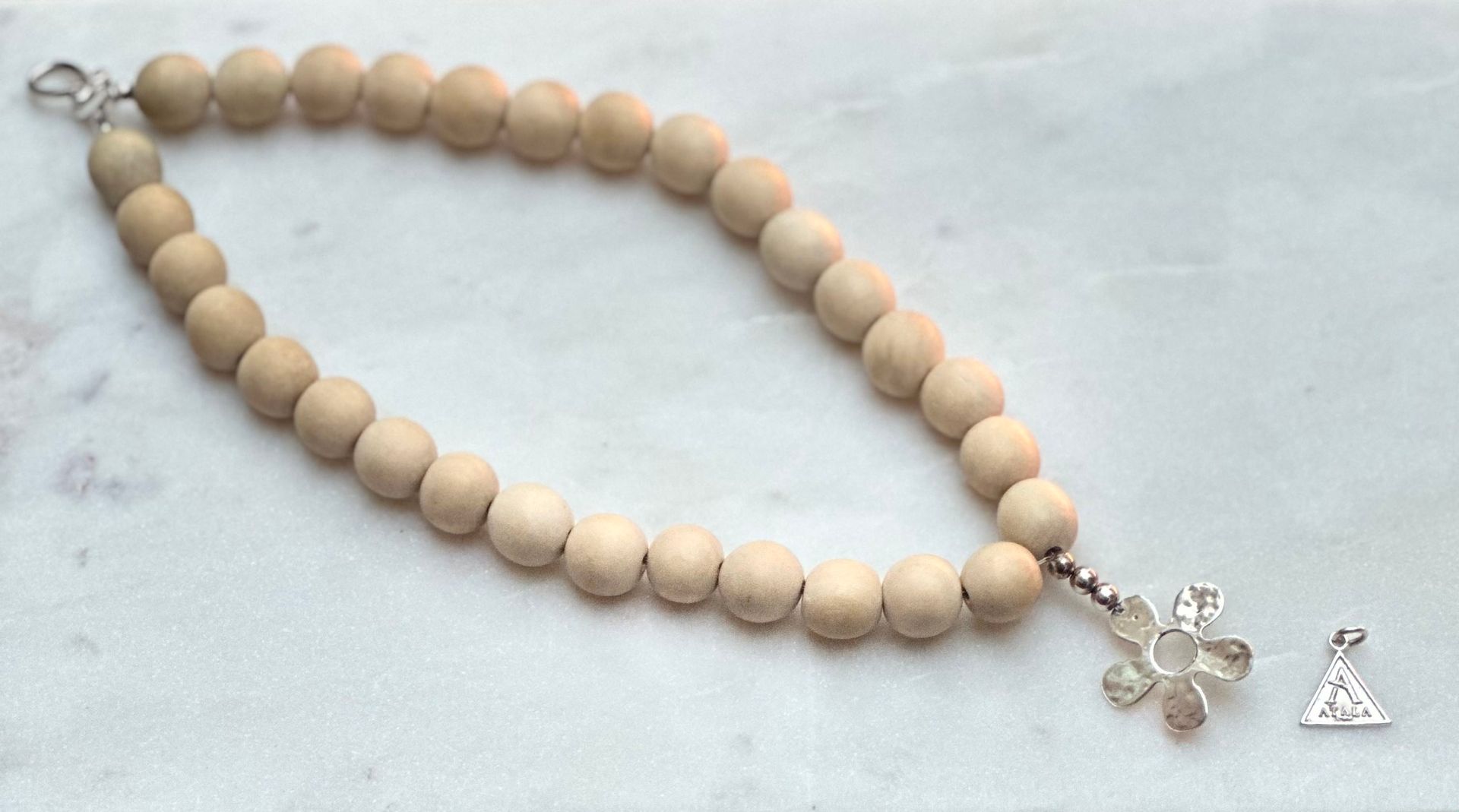 Beaded necklace with light wood beads and silver flower pendant. Small triangle charm to the side.