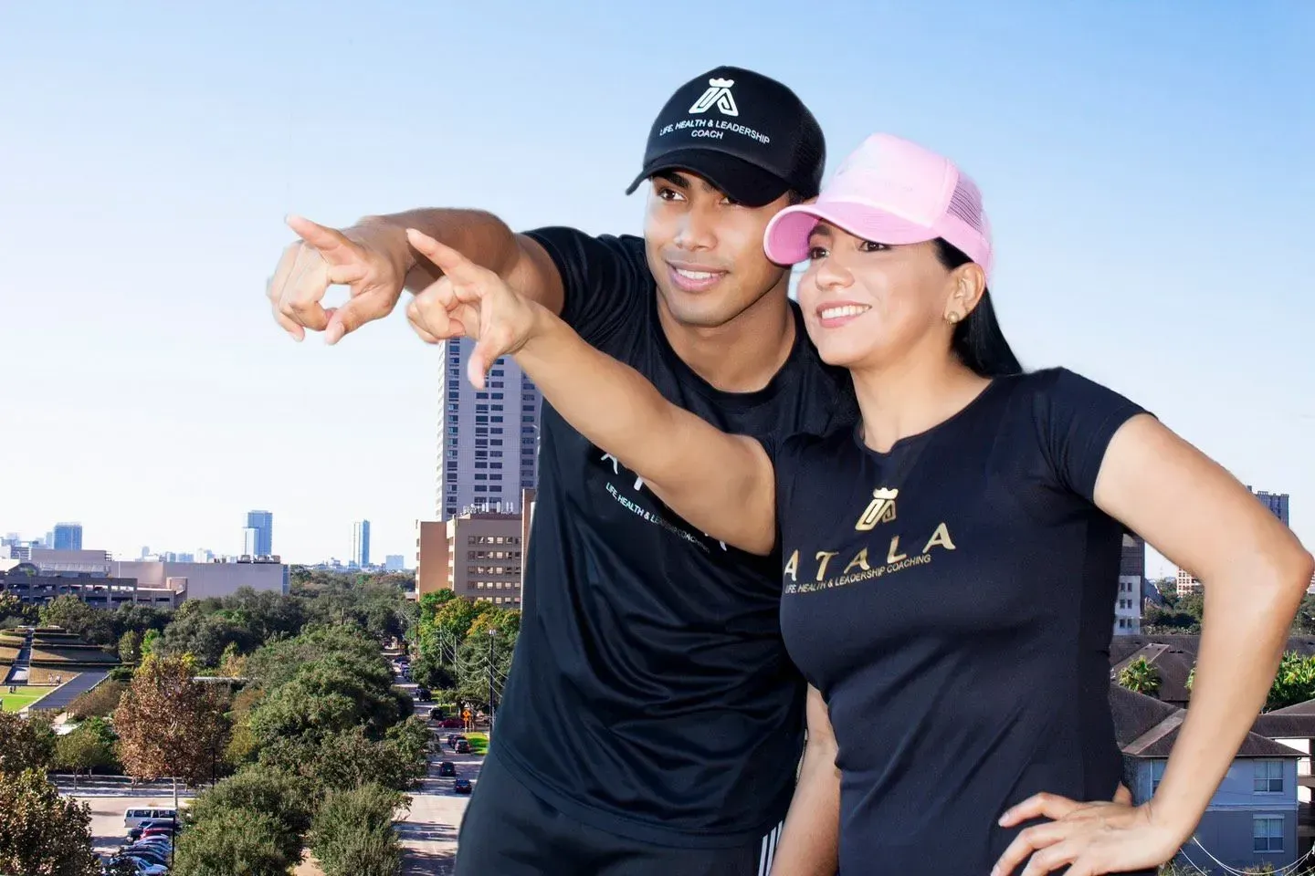 Man and woman wearing black shirts and caps pointing at a city view.