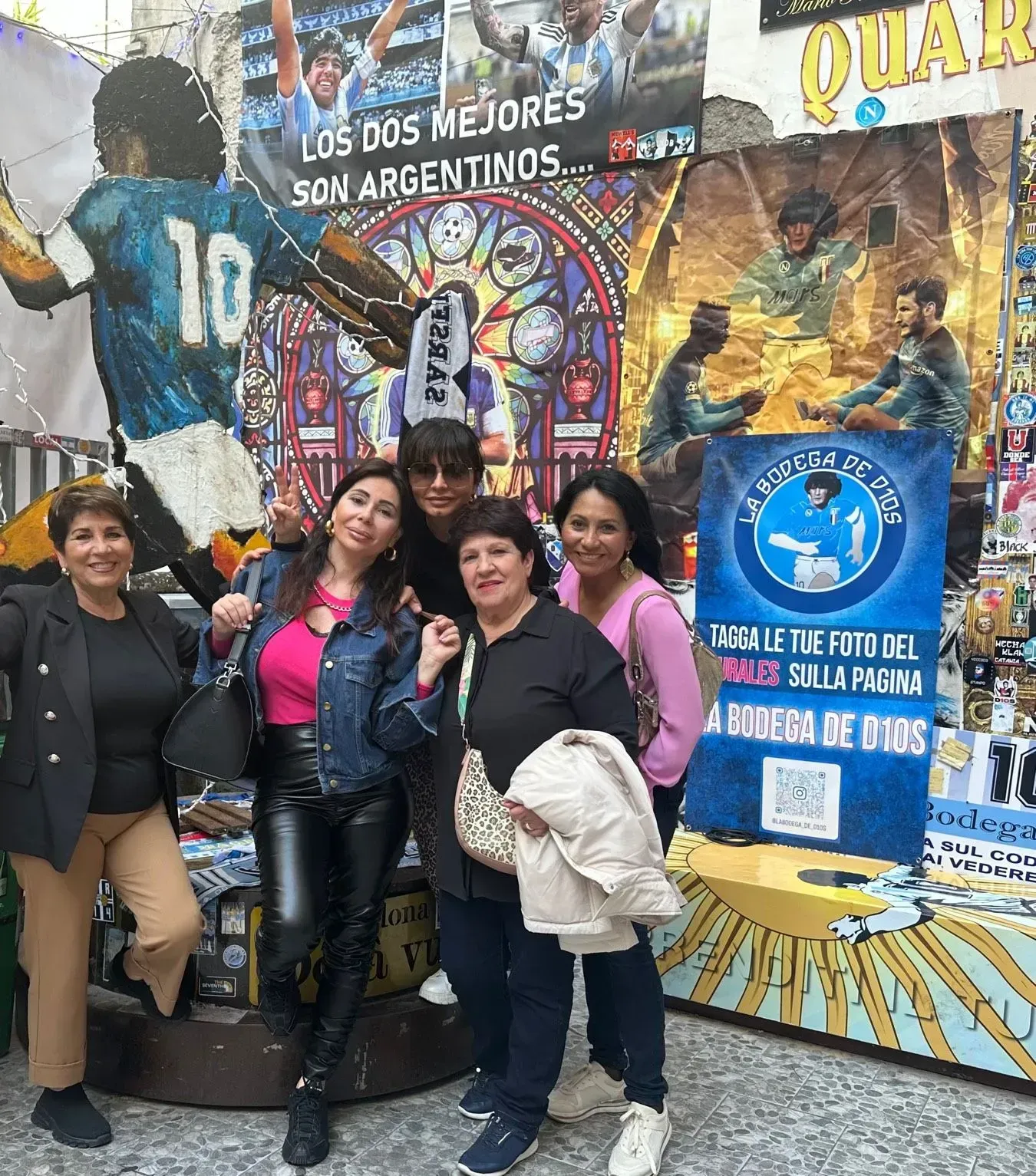 Group of five people posing in front of a colorful mural with text in Spanish, and a sign.