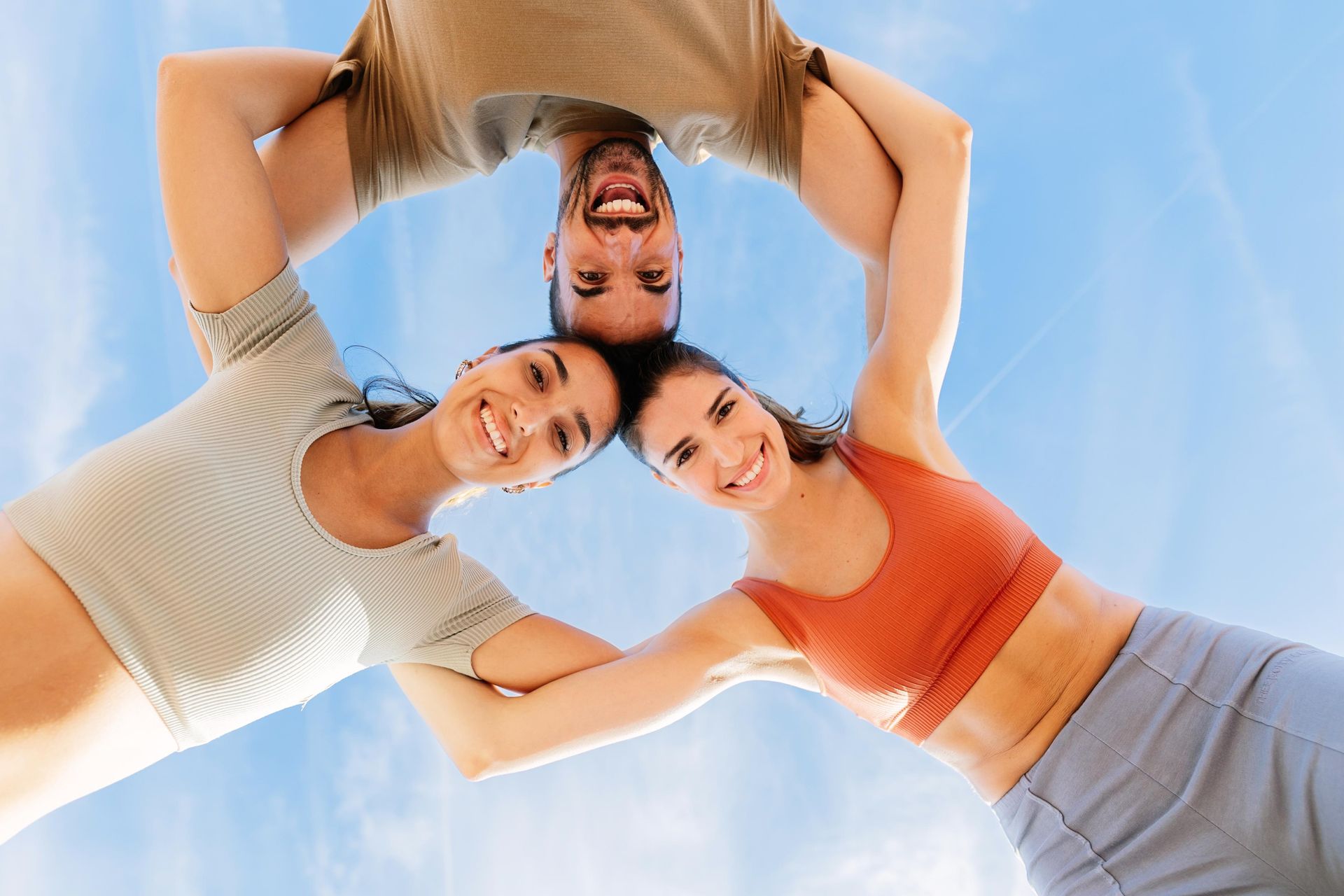 Three people smiling and holding hands, forming a circle against a blue sky.