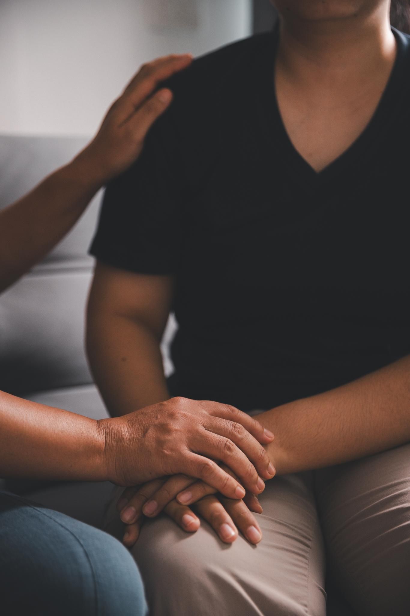 Two people, hands clasped, one hand on shoulder, offering comfort.