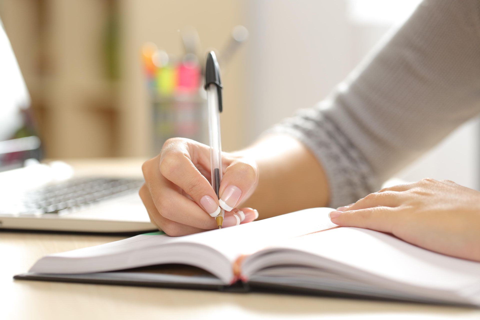 A person's hand with a pen writing in an open notebook on a desk.