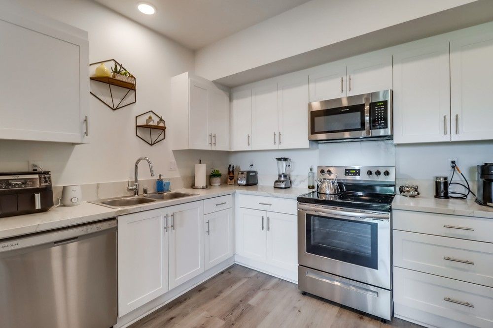 White kitchen with stainless steel appliances and light wood floors.