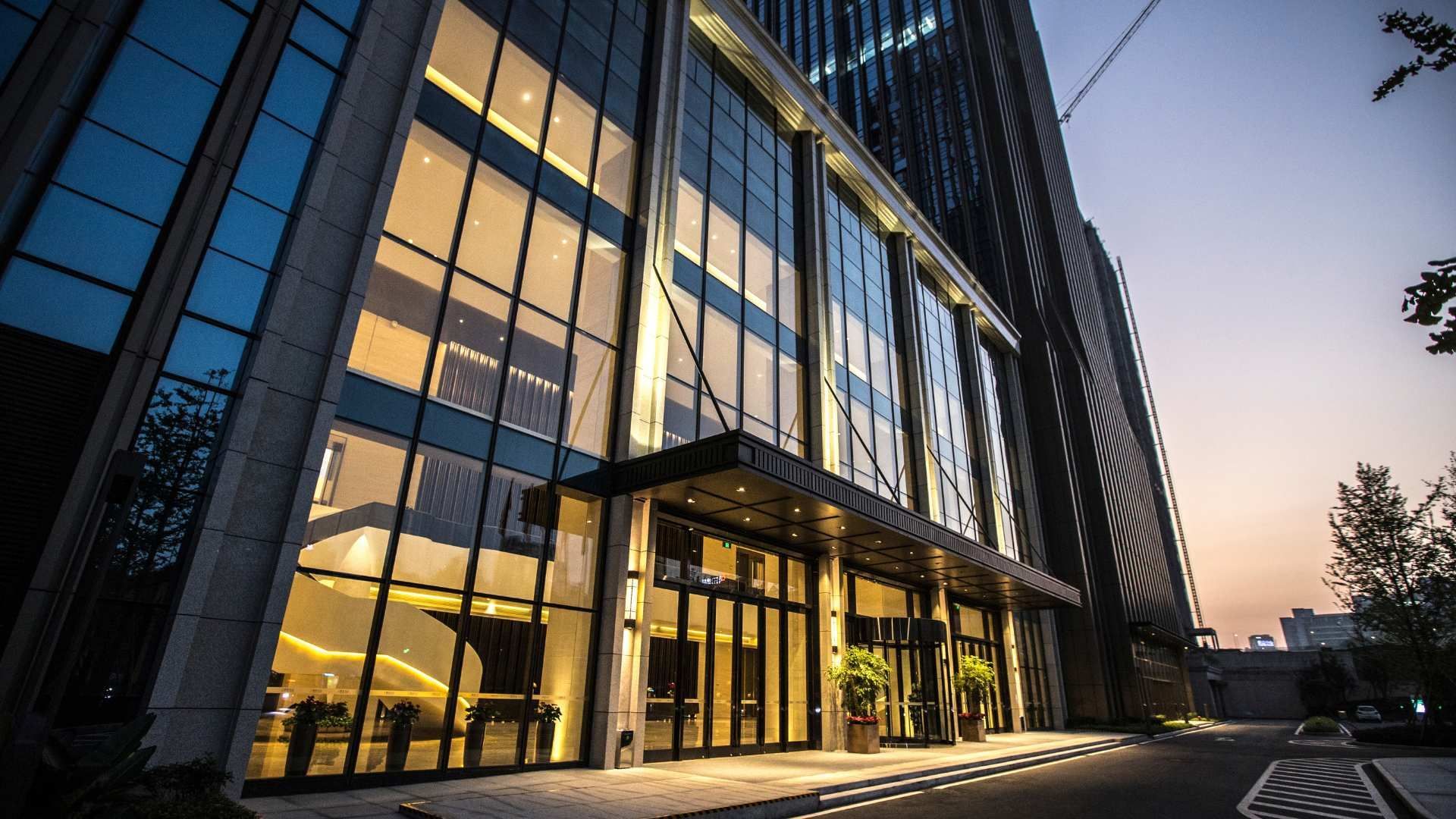 Modern glass office building at dusk with warm interior lights reflected on the facade
