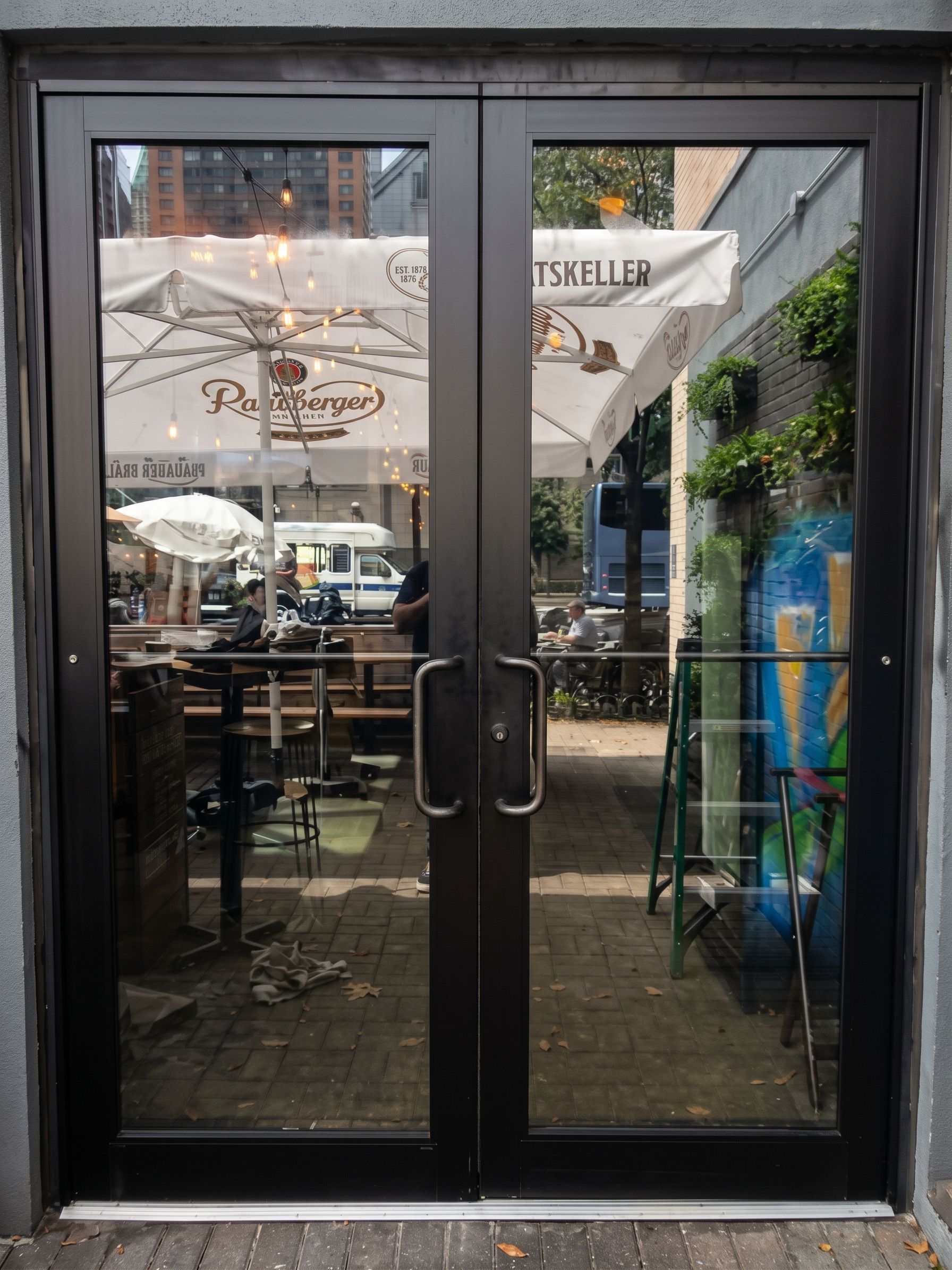 Glass double doors of a restaurant patio with tables and umbrellas visible inside and outside