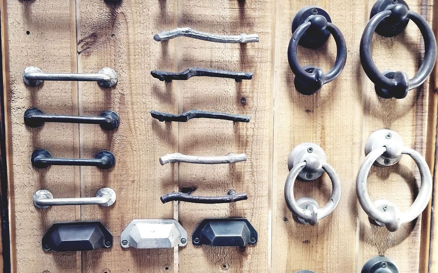 Assorted metal and plastic wall hooks in rows on a light wooden board.
