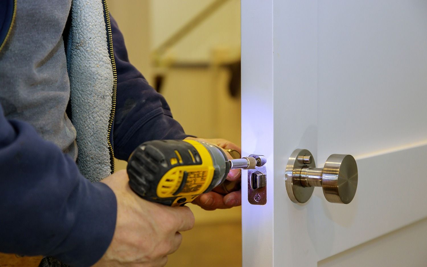 Person drilling a door latch with a yellow cordless drill while installing a knob
