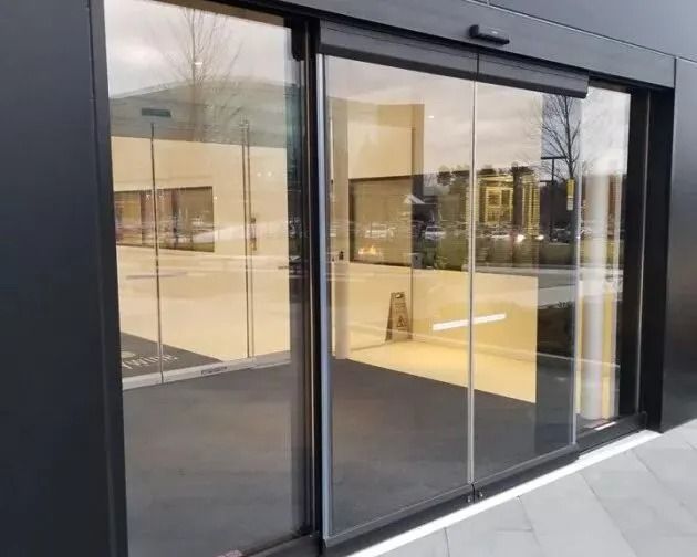 Glass automatic door with metal handles and a yellow “CAUTION” sticker reading “Automatic door” and “Activate switch to operate.”