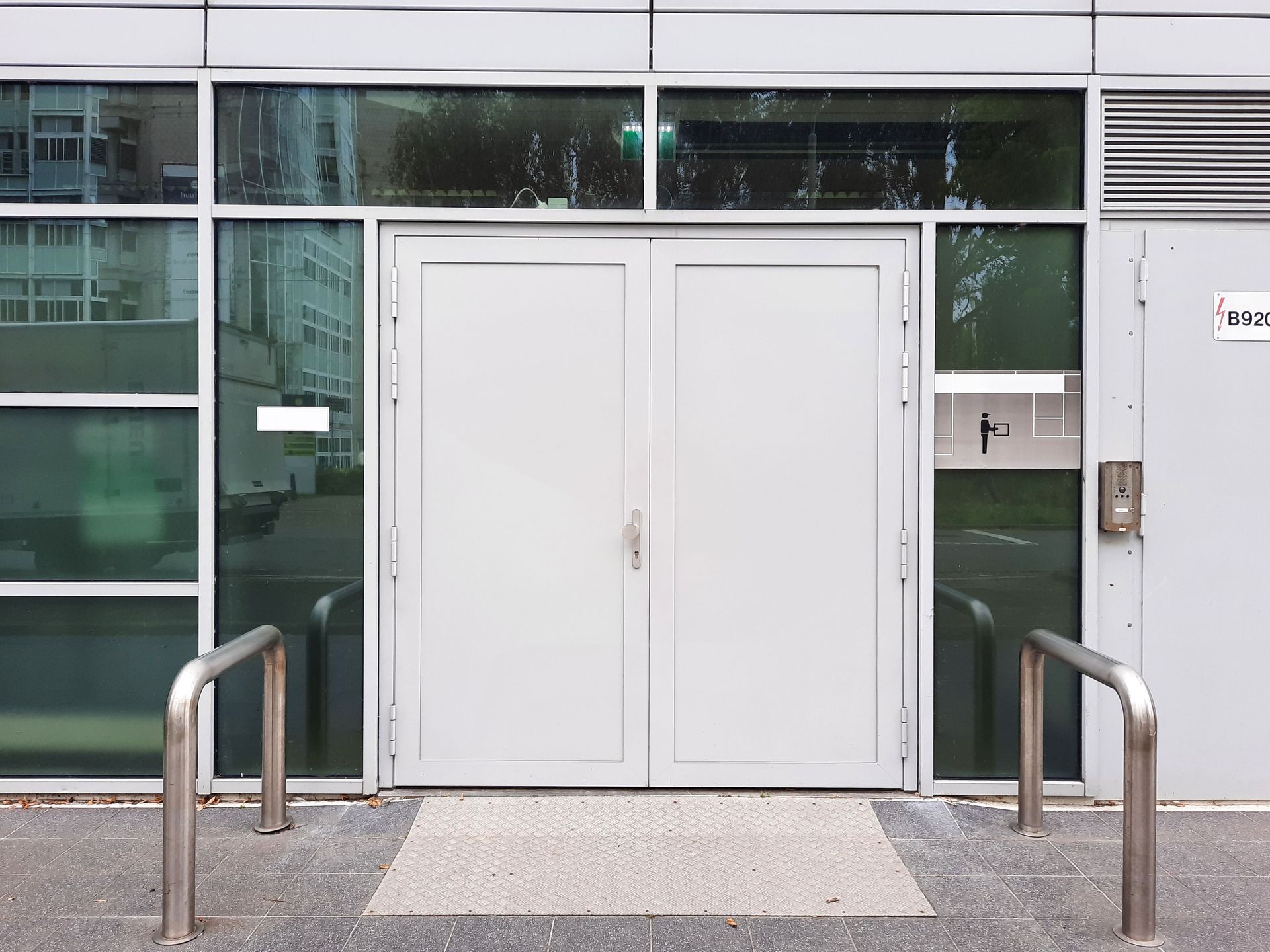 Glass entrance doors beside a brick wall, with sunlight reflecting on the building facade.