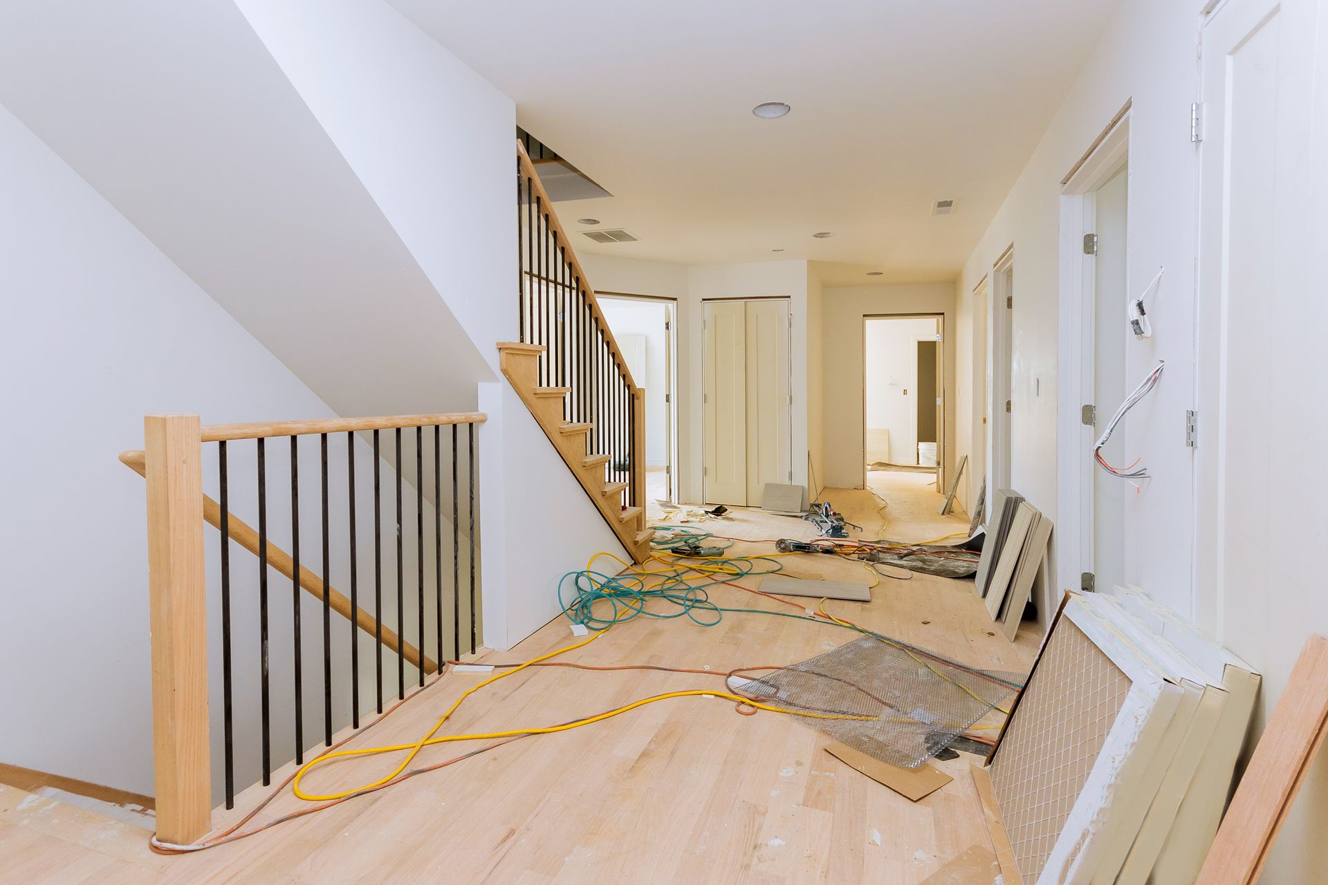 Hallway under construction; unfinished wooden floors and staircase, exposed wires, and white walls.