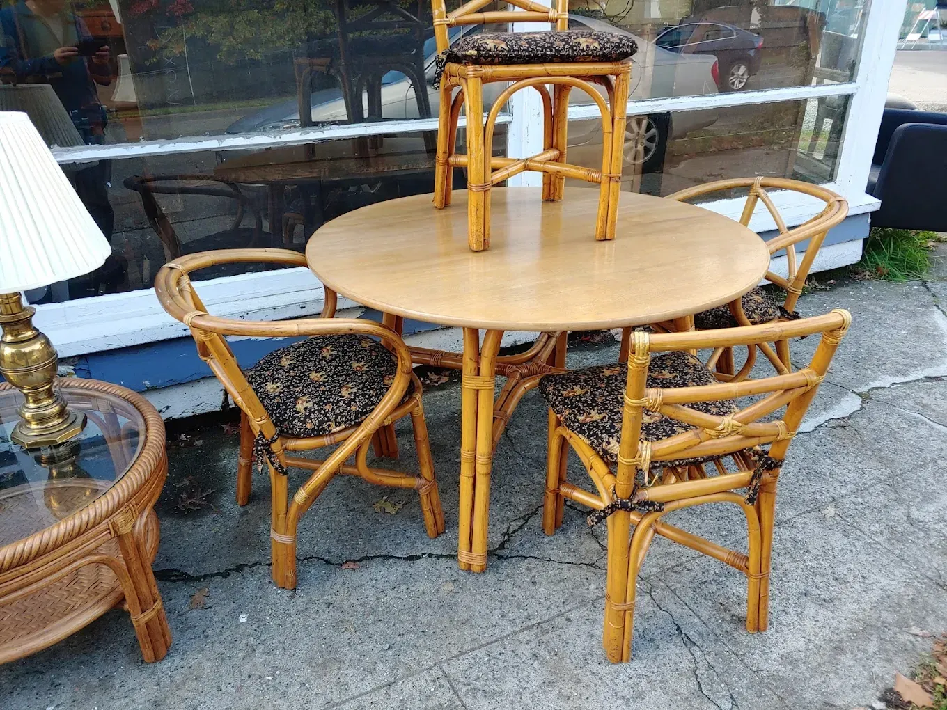 Small round wooden table with three wicker chairs on a sidewalk outside a shop window