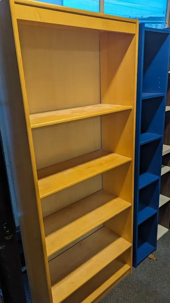 Yellow empty bookshelf with four shelves, next to a blue shelving unit in a store aisle