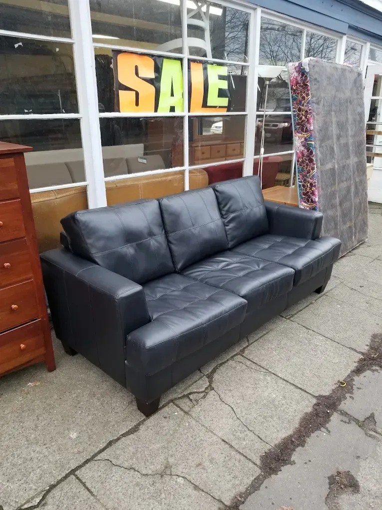 Black leather sofa outside a storefront window with a yellow SALE sign behind it