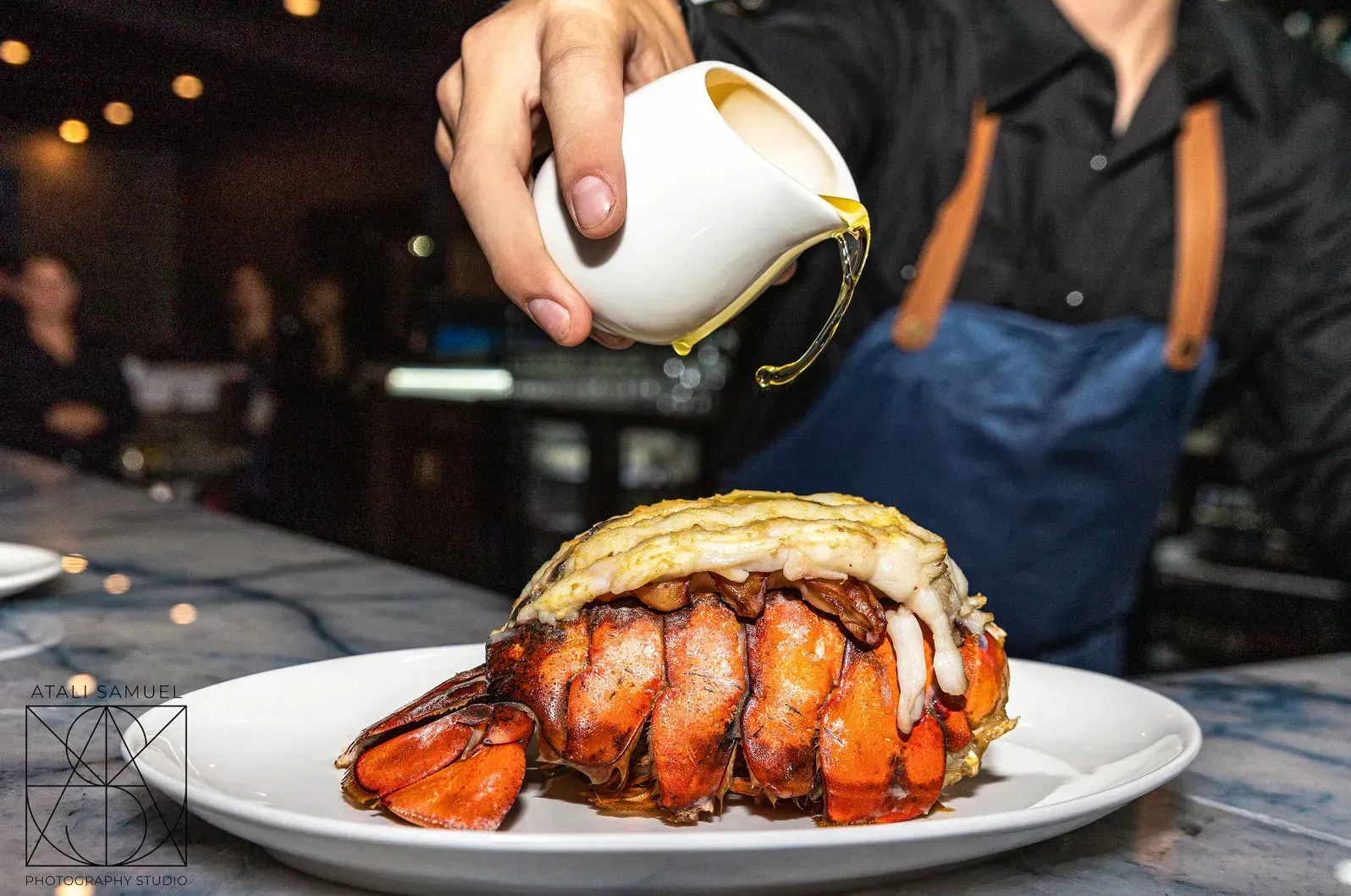 A chef pouring sauce over a lobster tail on a plate at a restaurant.