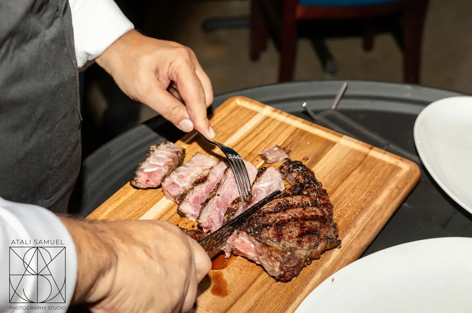 Hands slicing steak on a wooden board at a dining table