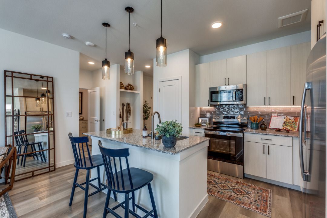 A kitchen with white cabinets , stainless steel appliances , a large island and a mirror.