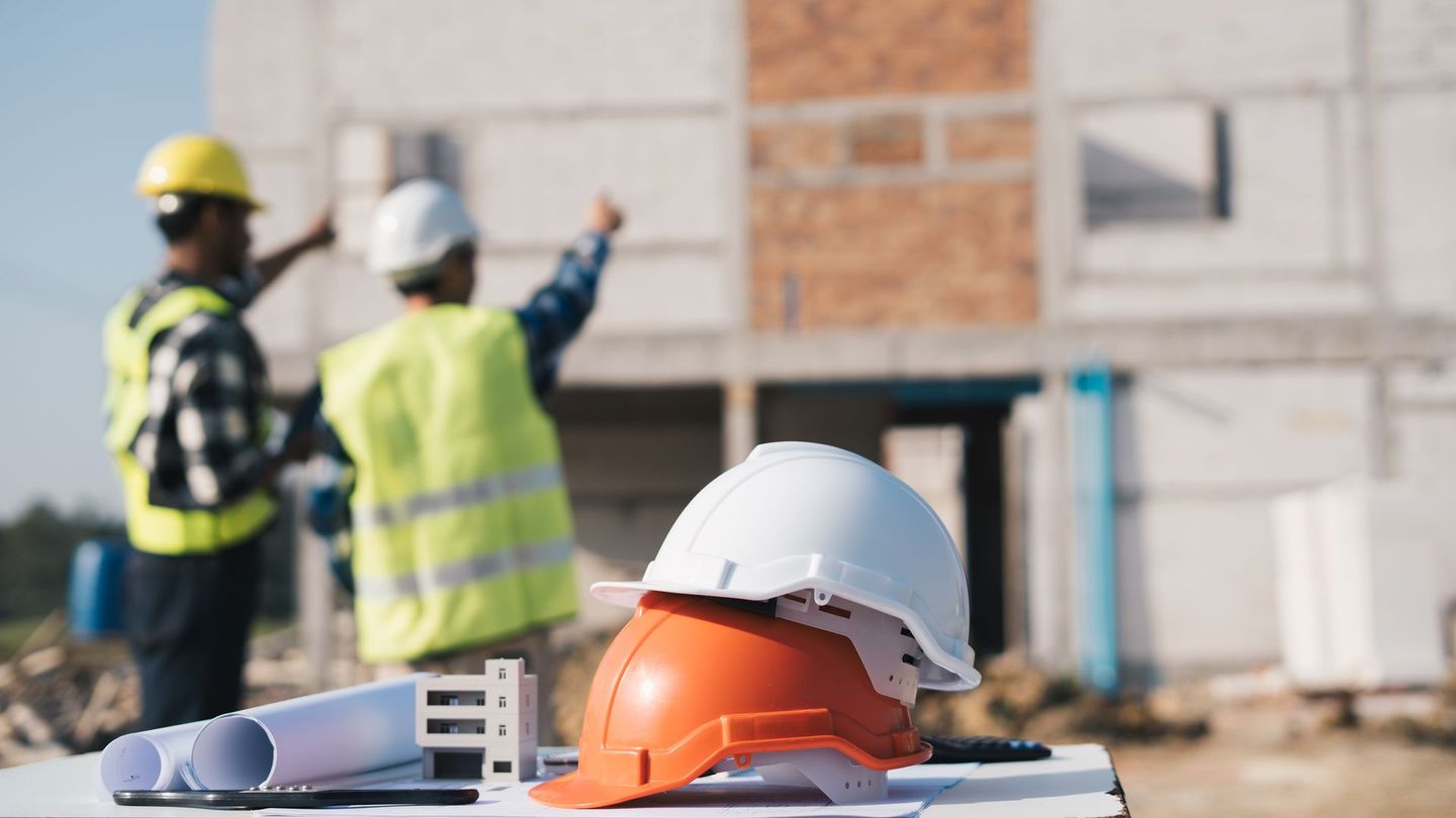 Operai edili in un cantiere, con caschi protettivi, progetti e indicazioni sulla struttura incompiuta.
