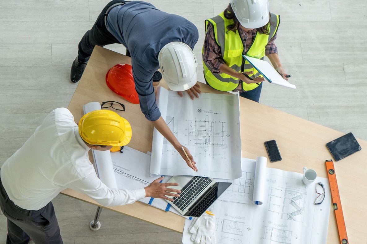 Gli operai edili con i caschi da cantiere esaminano i progetti seduti a un tavolo, discutendone i piani.