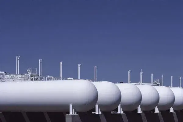 A row of white propane tanks are lined up against a blue sky.