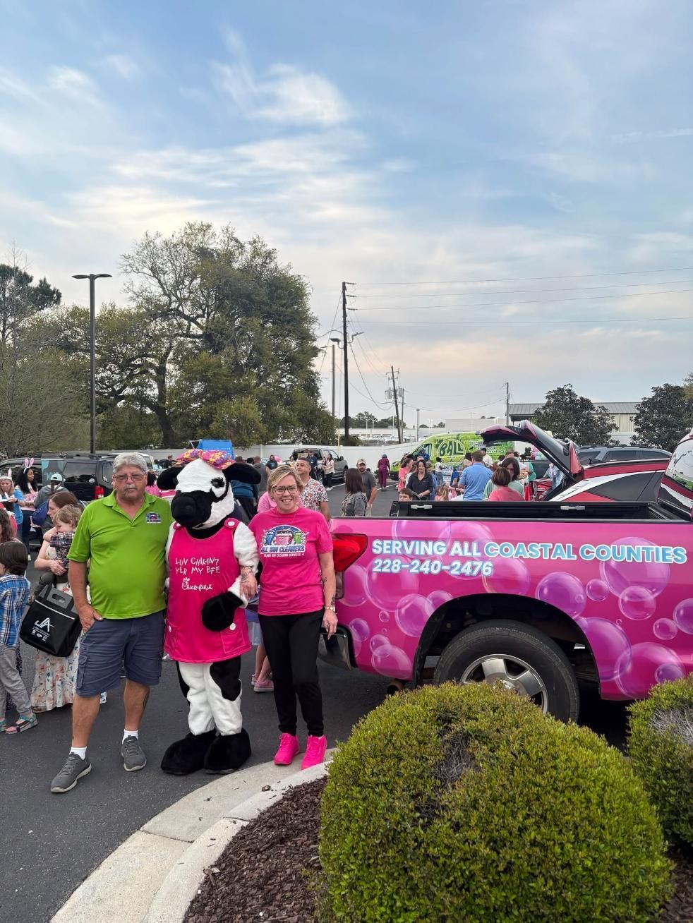People posing with a pink police truck in a parking lot during a community event