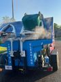 Blue cleaning machine spraying water onto a car in a parking lot under bright sun.