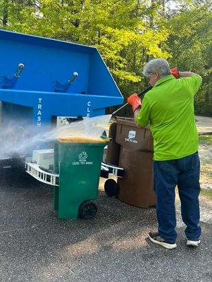 Worker in green shirt pours trash into a blue recycling truck beside bins on a street
