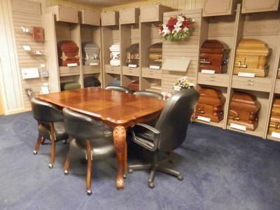 A funeral home showroom featuring a wooden conference table, chairs, and multiple caskets displayed on wall shelving.