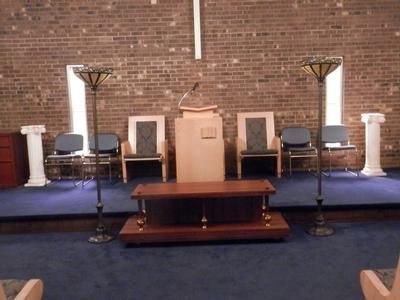 A church sanctuary altar featuring a central wooden pulpit, surrounding chairs, two floor lamps, and a wooden table.