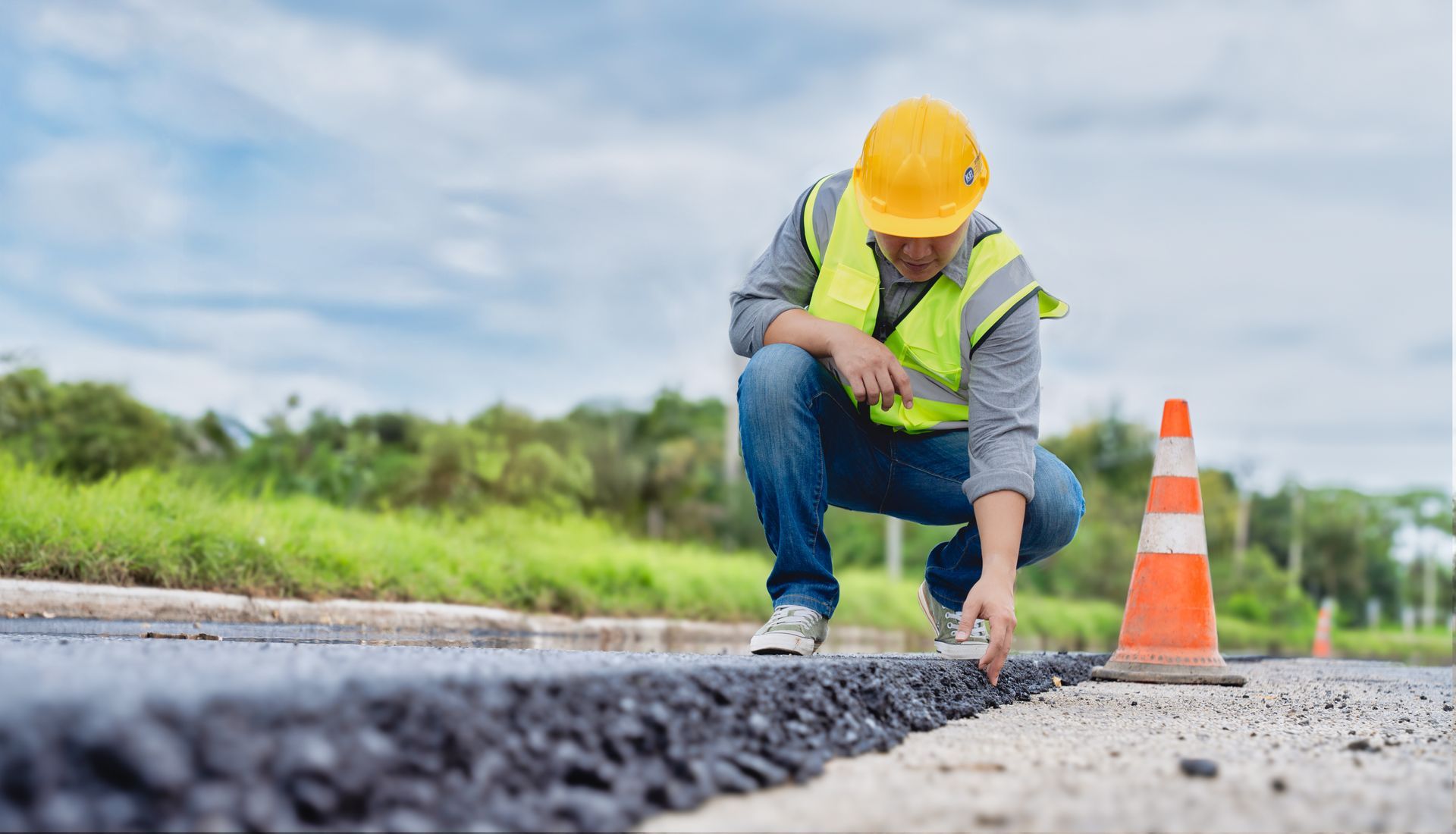 A male contractor checks a layer of asphalt on the ground while crouching.
