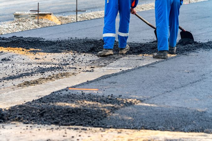 Road workers spreading hot asphalt to repair road surface during street paving construction project.