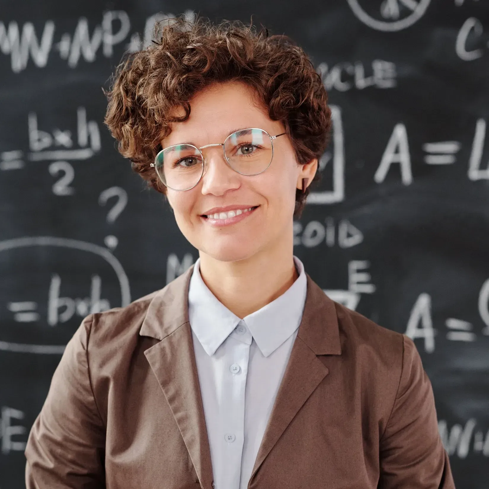 Woman smiling in front of a chalkboard with math equations written on it.