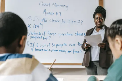 Teacher explaining math problems on a whiteboard to students in a classroom.