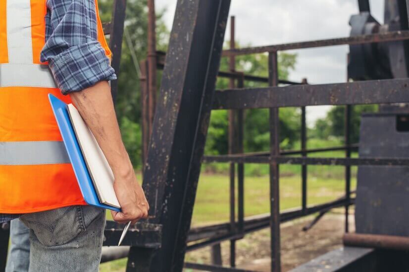 Worker in orange safety vest holding a clipboard beside a black metal gate outdoors