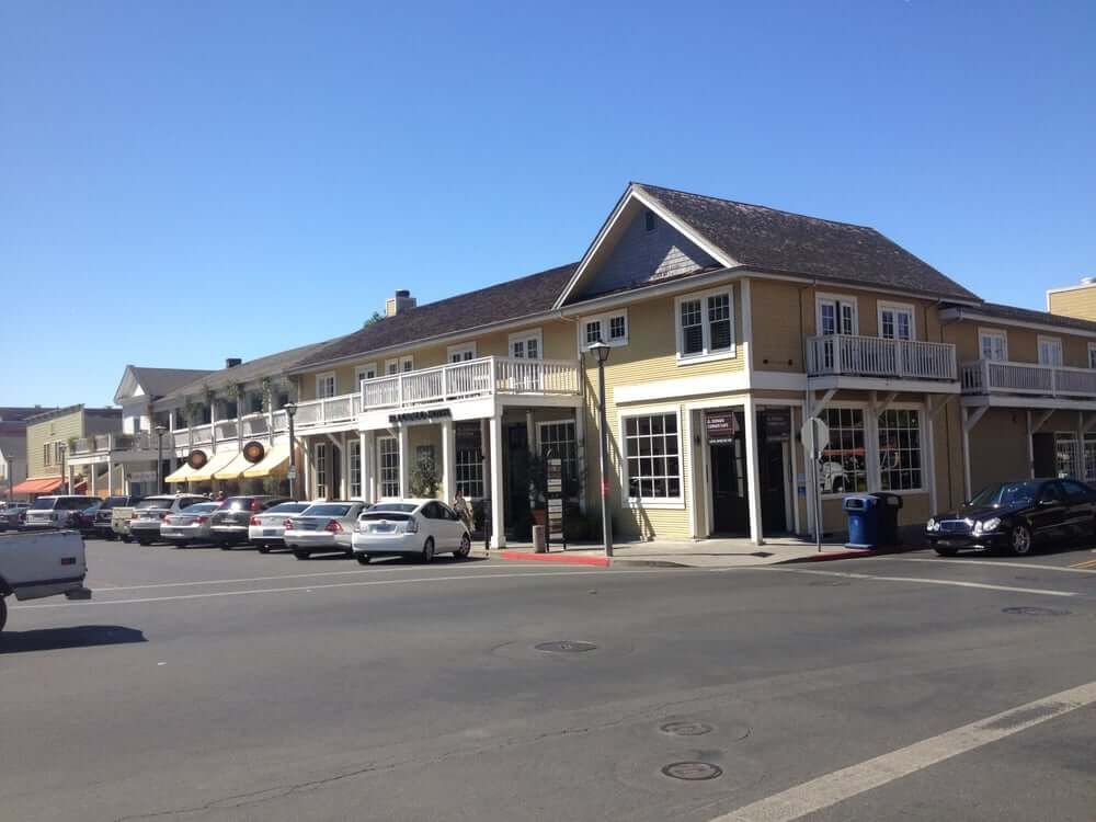 Street corner with parked cars and a tan two-story building on a sunny day