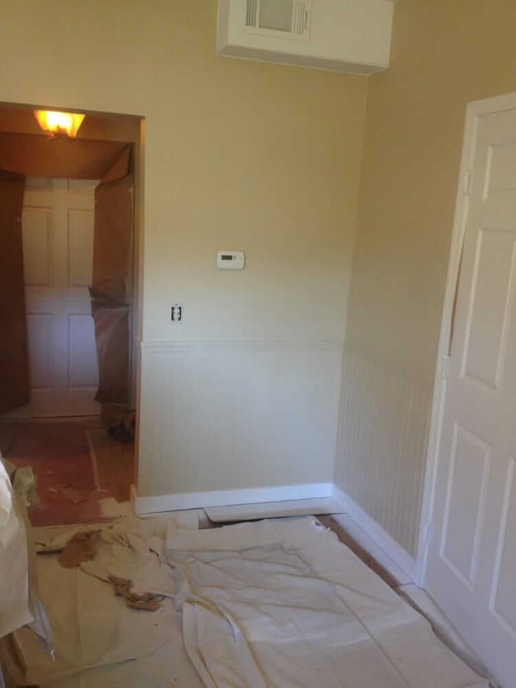 Partially renovated hallway with covered floor, doorway, wall thermostat, and closet doors