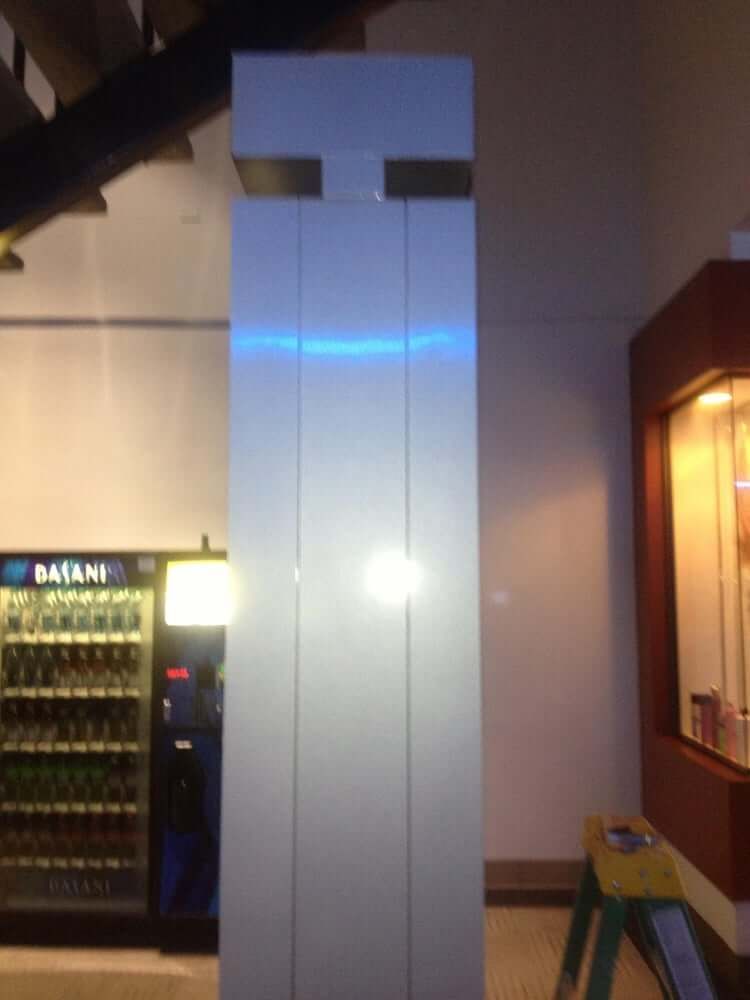 Tall white column with blue light inside a hallway beside vending machines and a wooden counter