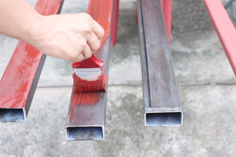 Hand painting red metal bars beside unpainted gray square tubes