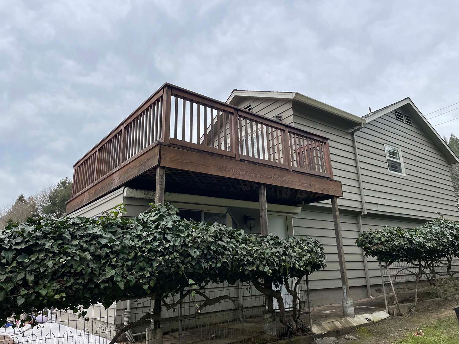 Raised wooden deck attached to a gray house, with shrubs along the side yard