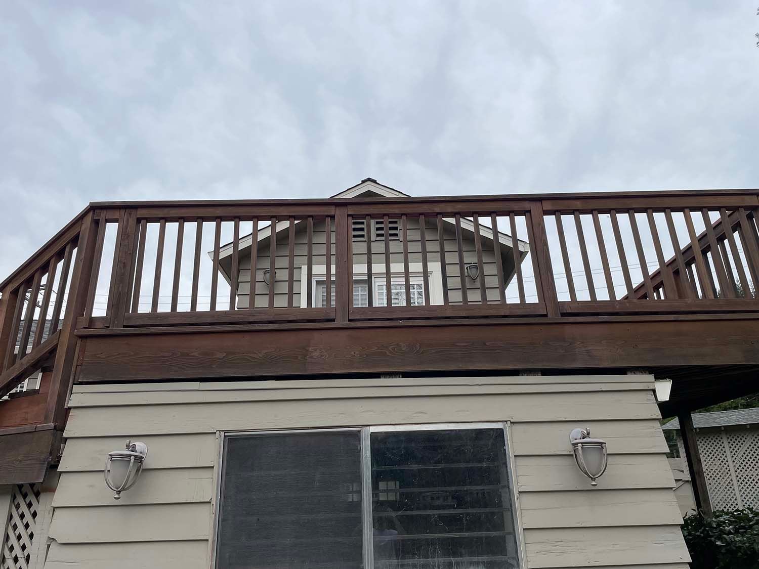 House with deck and railing viewed from below against cloudy sky