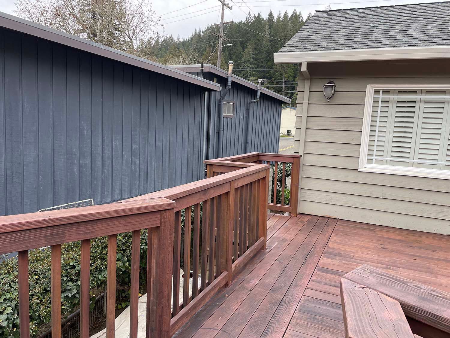 Wooden deck with red railings beside a beige house and blue shed, viewed from the corner.